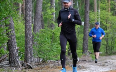 Outdoor exercise scene with two men jogging through a lush green forest trail, wearing sports attire.